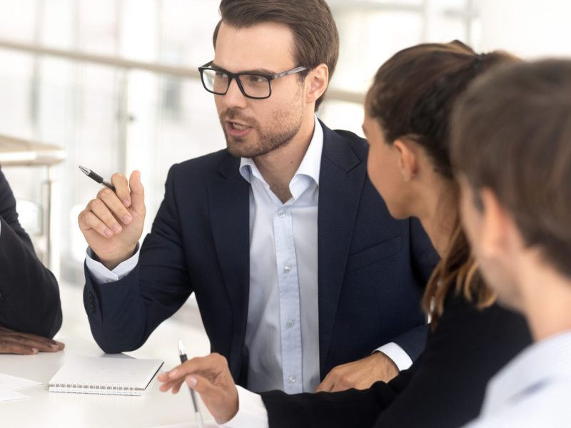 Businessman,Coach,Speaking,At,Diverse,Group,Meeting,Sit,At,Table